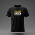 Front view: Black t-shirt floating on a grey background with 'Jugaad Driven Development' as a justified stack printed across the chest in off-white and amber.