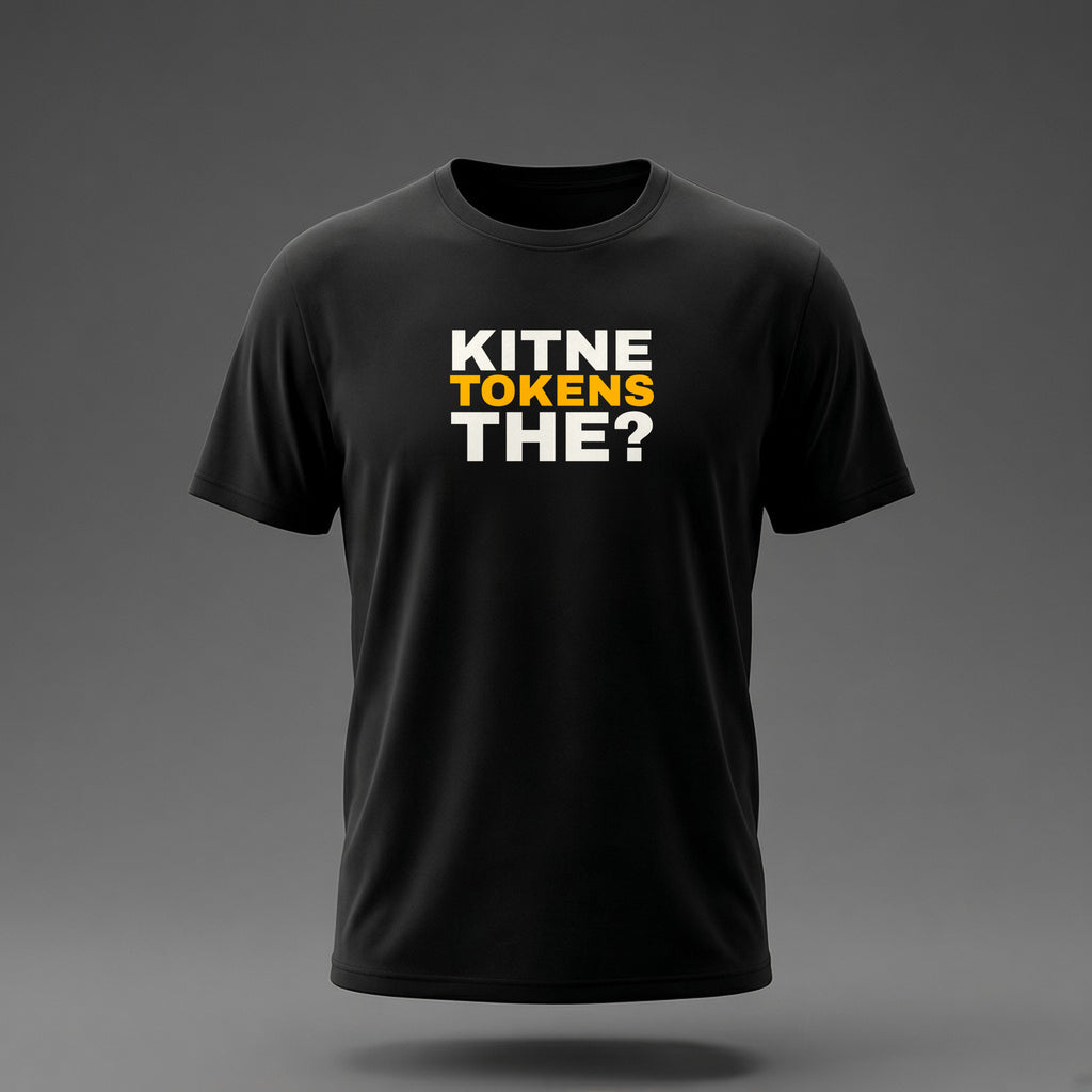 Front view: Black t-shirt floating on a grey background with 'Kitne tokens the?' as a justified heavy stack printed across the chest in off-white and amber.