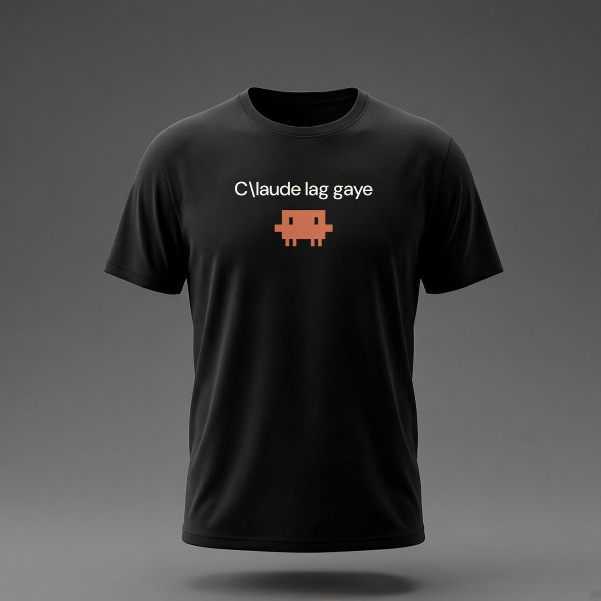 Front view: Black t-shirt floating on a grey background with a single short lowercase line of off-white text across the chest and a small coral pixel-art critter below it.
