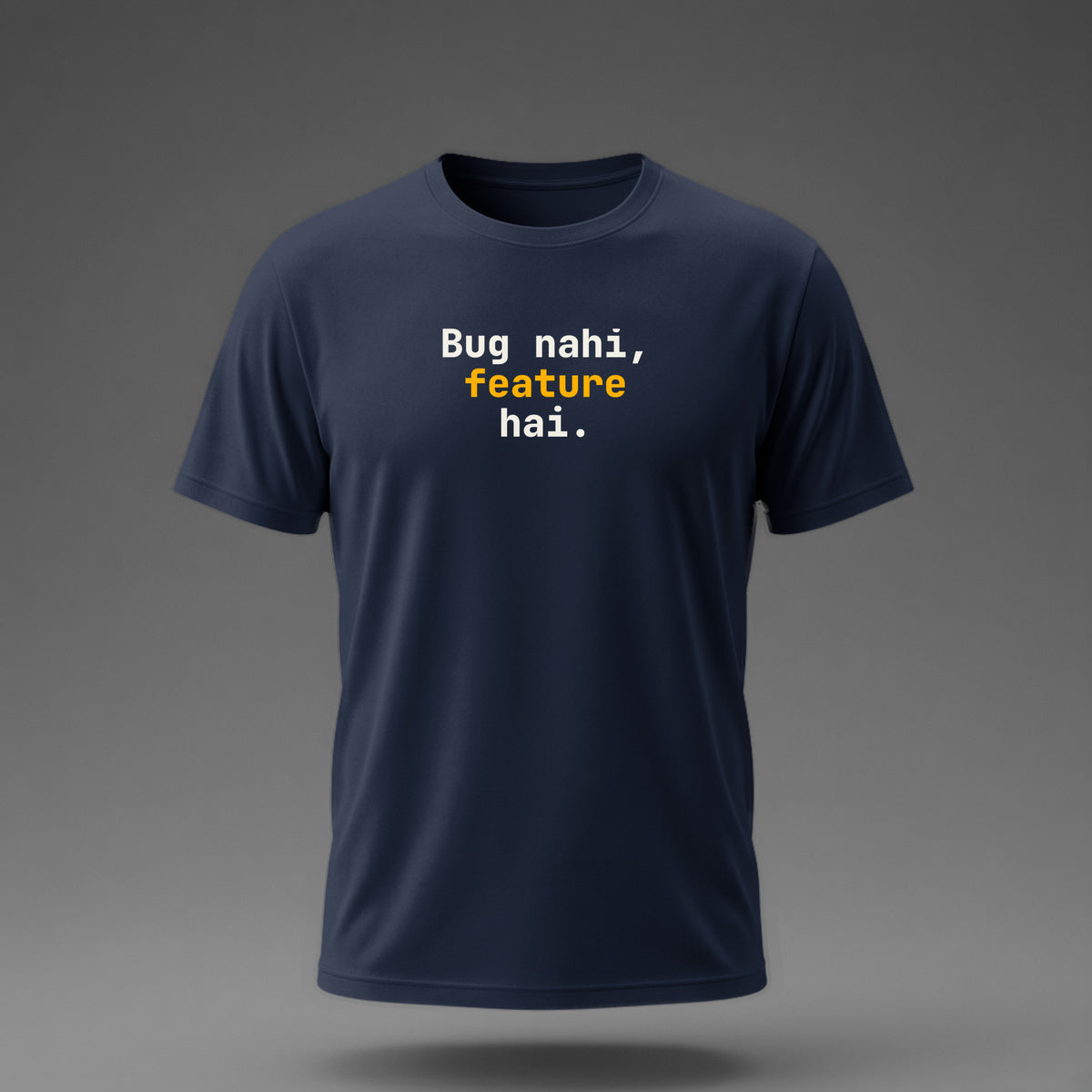 Front view: Navy t-shirt floating on a grey background with 'Bug nahi, feature hai.' in three heavy mono lines printed across the chest in off-white and amber.