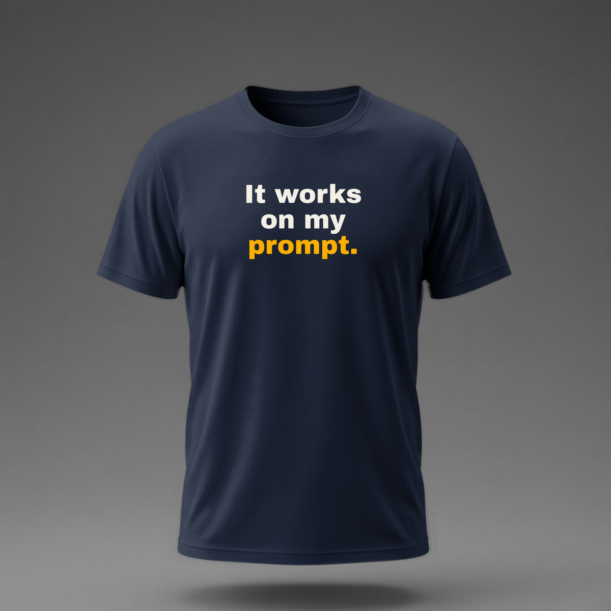 Front view: Navy t-shirt floating on a grey background with 'It works on my prompt.' in three heavy lines printed across the chest in off-white and amber.