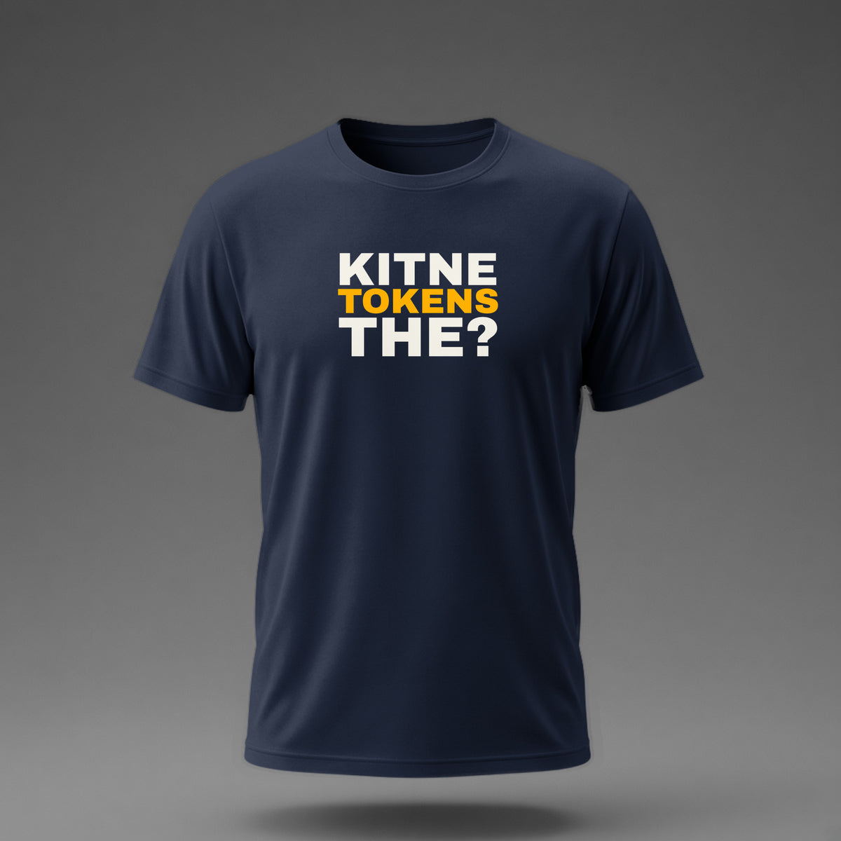 Front view: Navy t-shirt floating on a grey background with 'Kitne tokens the?' as a justified heavy stack printed across the chest in off-white and amber.