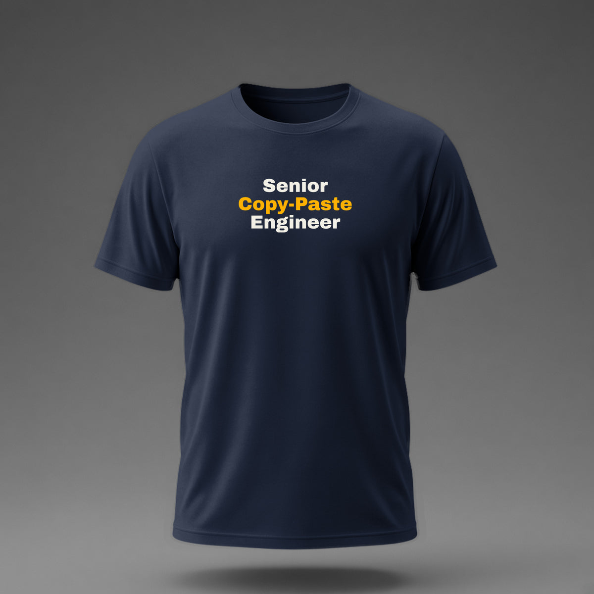 Front view: Navy t-shirt floating on a grey background with 'Senior Copy-Paste Engineer' in three heavy lines printed across the chest in off-white and amber.