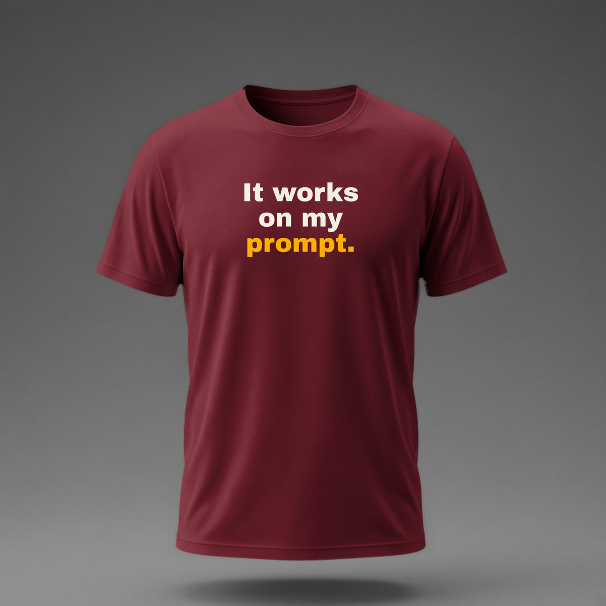 Front view: Maroon t-shirt floating on a grey background with 'It works on my prompt.' in three heavy lines printed across the chest in off-white and amber.