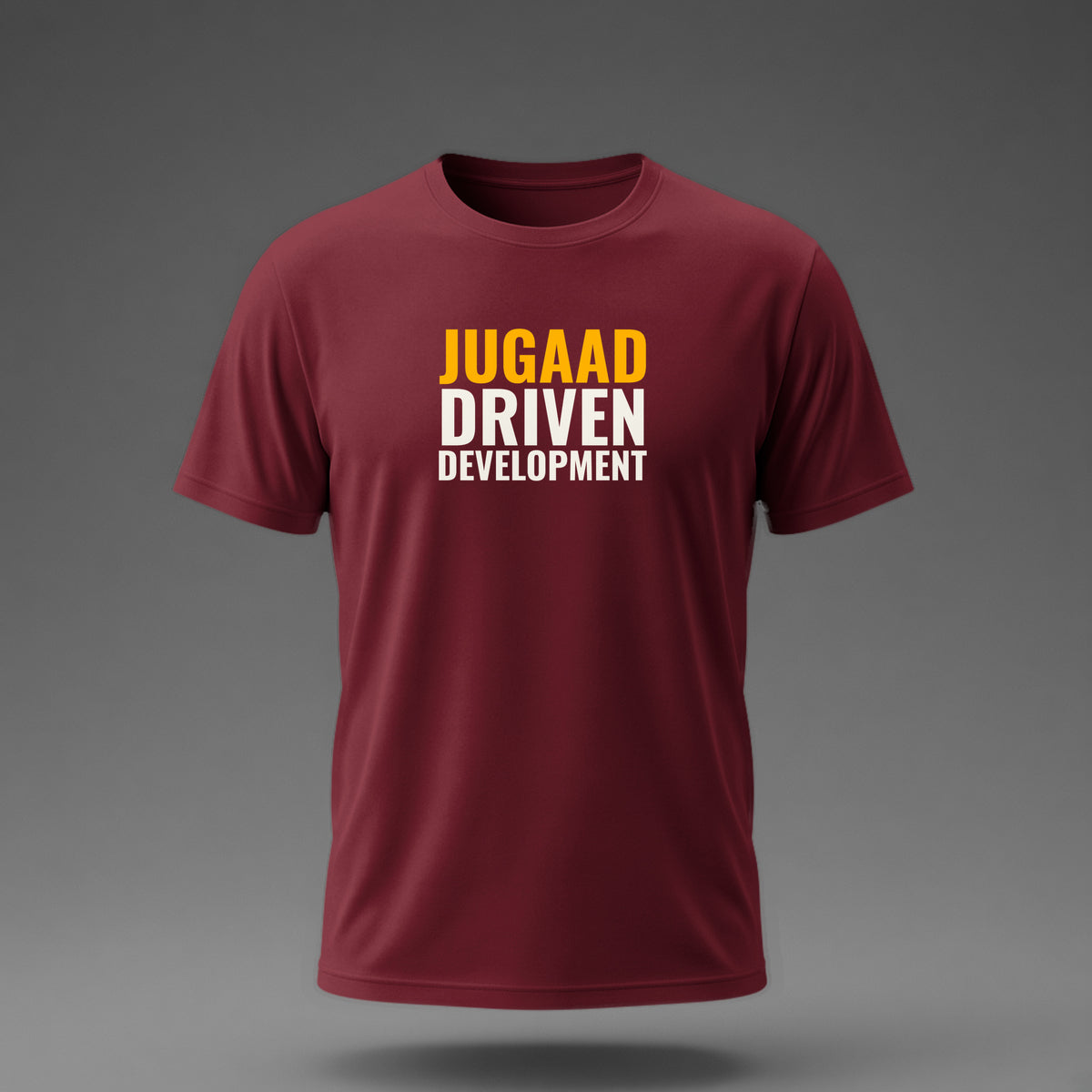 Front view: Maroon t-shirt floating on a grey background with 'Jugaad Driven Development' as a justified stack printed across the chest in off-white and amber.