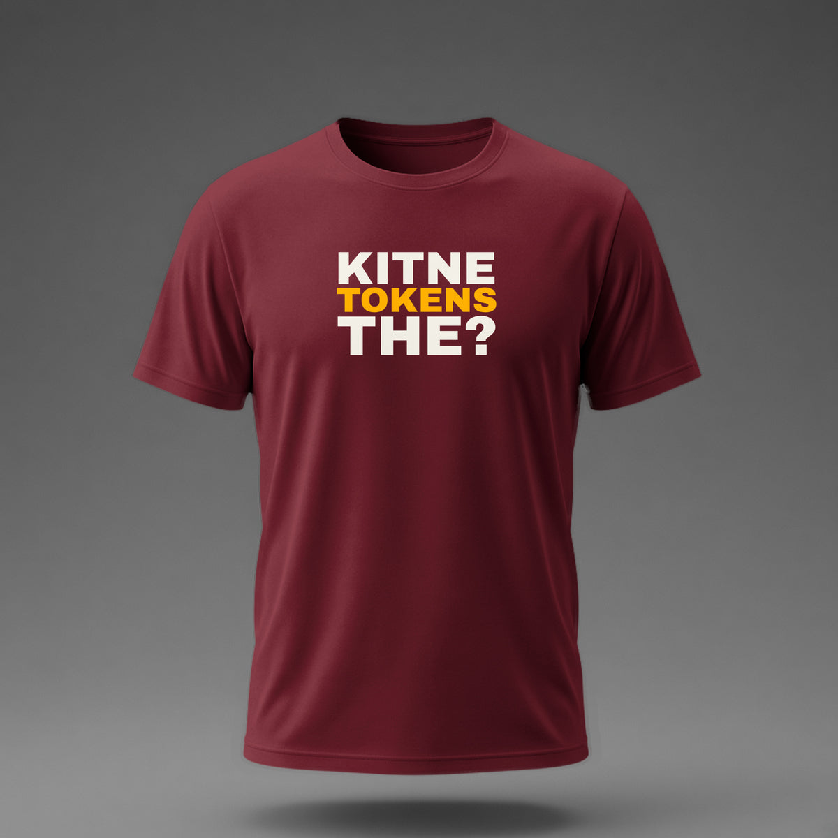 Front view: Maroon t-shirt floating on a grey background with 'Kitne tokens the?' as a justified heavy stack printed across the chest in off-white and amber.