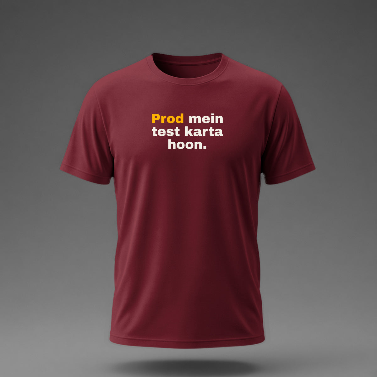 Front view: Maroon t-shirt floating on a grey background with 'Prod mein test karta hoon.' in three heavy lines printed across the chest in off-white and amber.